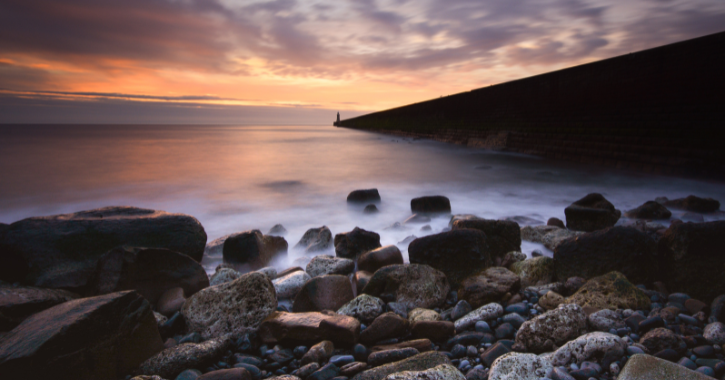 View of Tynemouth Pier and the North Sea under a pink and orange sky.